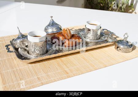 Arabic coffee cups served with fresh dates in sunlight. Stock Photo
