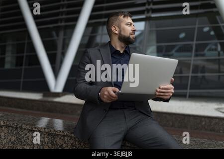 Man in business suit sitting working on laptop outside Stock Photo