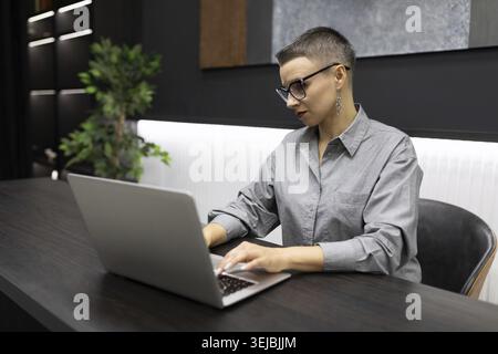 Successful woman programmer working in a stylish office behind a laptop developing a new application Stock Photo
