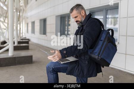 Mature male entrepreneur working on laptop online in airport lounge Stock Photo
