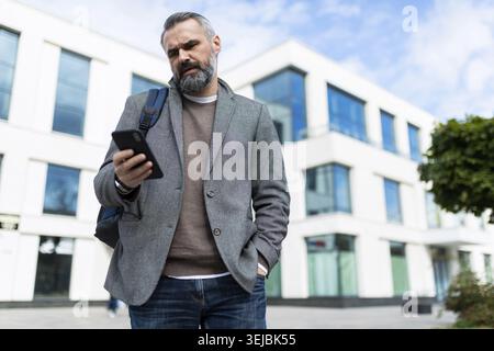 Adult male software engineer leaves the office and looks at the mobile phone Stock Photo
