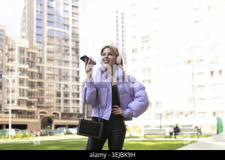 Caucasian woman 40 years old in headphones speaks on a mobile phone hands-free outside Stock Photo