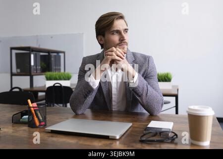 Stylish young businessman pensive sitting at the table in the office Stock Photo
