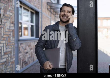 Middle-aged man programmer talking on a mobile phone with a laptop in his hands Stock Photo