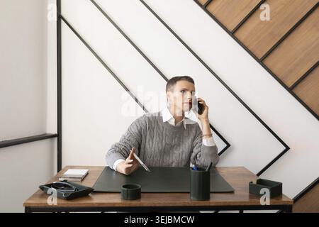 Business caucasian serious woman talking on mobile phone while sitting at table in office Stock Photo