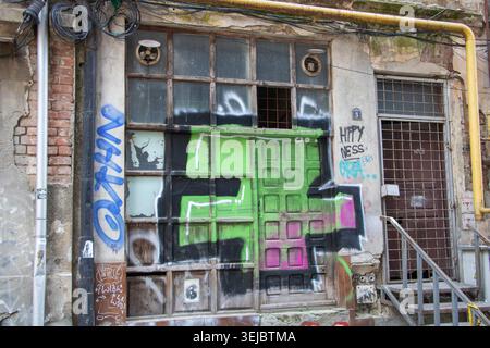 Old deteriorated urban building facade with broken windows, graffiti and weathered industrial doorway in Bucuresti, Romania - March 15 2026 Stock Photo