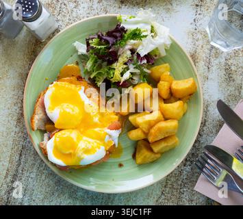 Eggs Benedict with smoked salmon, fried potatoes and greens Stock Photo