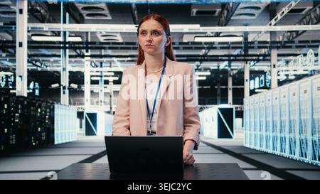 Monitoring rigs power consumption, laptop and woman at server hub workplace desk. Overseeing equipment, notebook and employee in data center ensuring industry standards compliance, camera A Stock Photo
