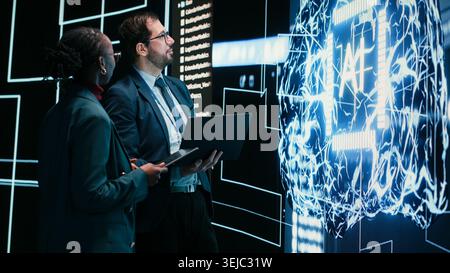 Engineering team looks at AI machine learning self writing code on screen, autonomy concept. Teamworking colleagues reviewing self sustaining artificial intelligence model, doing brainstorming Stock Photo