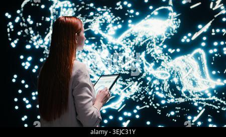 Software developer optimizes neural network neurons map with tablet and augmented reality tech. Female technician fine tuning AI model synaptic weights with touchscreen device, camera B Stock Photo