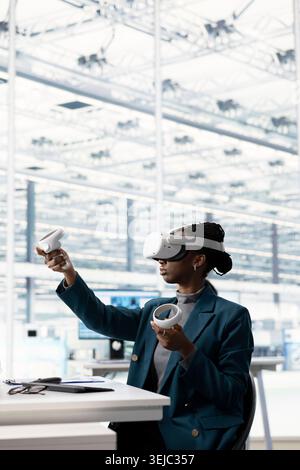 Female engineer using VR glasses to do microchip yield enhancement, tracking defects data. African american IT expert monitoring PCB production in factory office using virtual reality simulation Stock Photo
