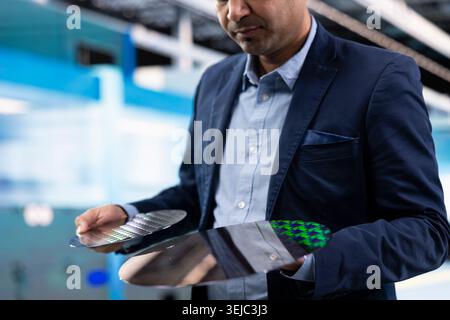 Comparing silicon wafers, semiconductors and Indian man inside high tech manufacturing plant. Innovating microelectronics technology, microchip substrate and management executive in factory Stock Photo