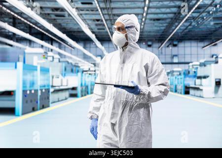 Wearing bunny suit, tablet application and hardware designer in microchip industrial plant. Automating production lines systems, device app and worker in semiconductor factory Stock Photo