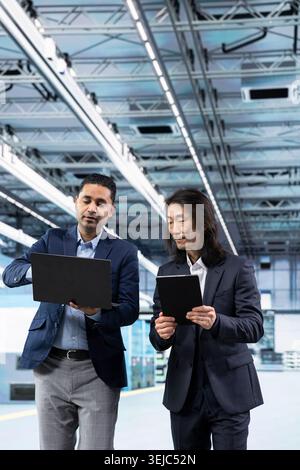 Working together, microchip and multiethnic men in factory talking, comparing components production metrics. Analyzing semiconductors, PCB production plant data and teamworking management executives Stock Photo