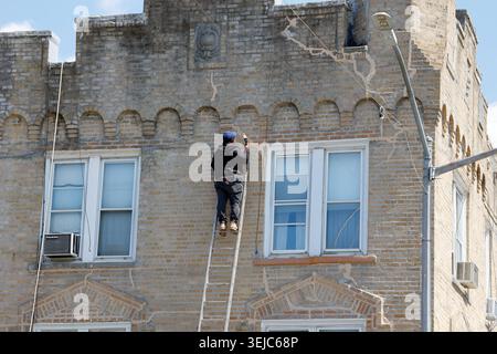 A worker on an extension ladder covers cracks in a masonary brick wall of a NYC building with epoxy. Stock Photo