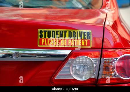 A "Student Driver Please Be Patient" reflective sticker on the trunk/boot of a red car driven by a person with a learner driving permit, or provisiona Stock Photo