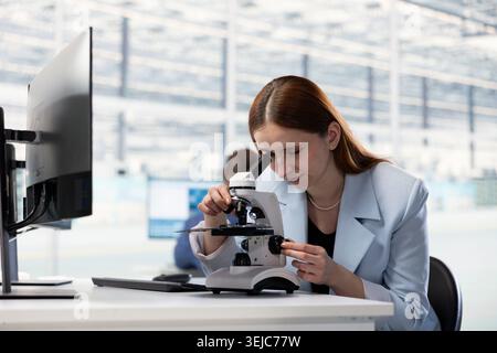 Researcher examining PCB circuitry with microscope, analyzing hardware components. Technician evaluating electronic prototypes with optical instrument in semiconductor manufacturing plant RD office Stock Photo