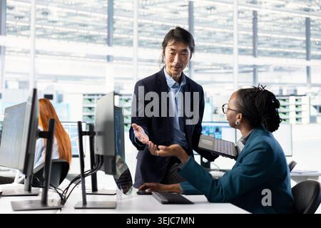Monitoring microchip production, yield quality and factory manager overseeing work done by female engineer in office. overseeing manufacturing, PCB parts and integrated circuit designer with coworker Stock Photo