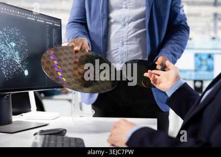 Close up of microchip designer inspecting silicon wafer substrates with AI deep learning. Experts using neural network tech to analyze semiconductor slice in manufacturing plant research facility Stock Photo