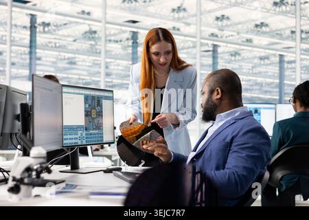 Inspecting silicon wafer substrates, research and multiethnic engineering team at office desk in industrial plant facility. Analyzing semiconductor slice, African american man and coworker Stock Photo