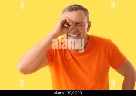 Mature man looking through imaginary telescope on yellow background Stock Photo