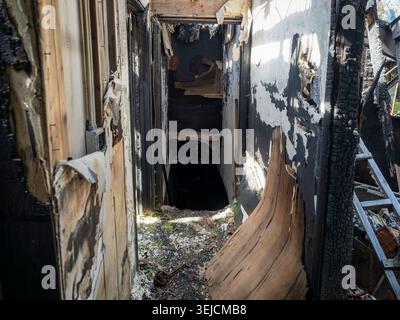 Interior view of a heavily charred hallway and door frame inside a building severely damaged by fire showing burnt wood and peeling walls Stock Photo