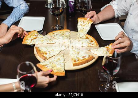 Top Angle View of Diverse Friends Hands Taking Slices of Cheesy Four Cheese Pizza in Restaurant During Dinner Stock Photo