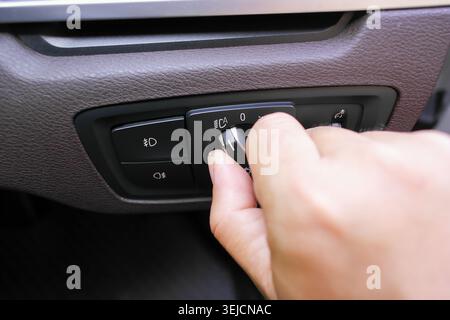 A hand turning the rotary headlight control switch on a car dashboard, illustrating automotive electronics, vehicle lighting controls, and driver cabi Stock Photo