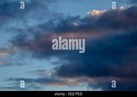 Dark brooding clouds with subtle warm tones against a pale blue sky Stock Photo
