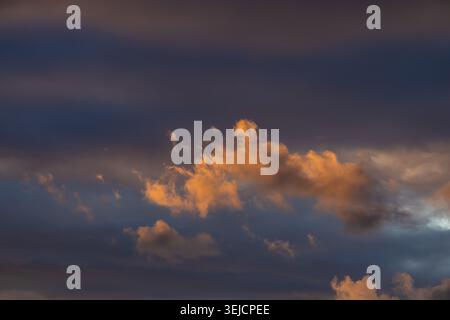 Golden-lit clouds against a deep blue sky at sunset Stock Photo
