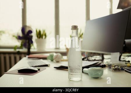 Close up of cold water bottle standing on office desk near computer, supporting workplace hydration and healthy routine. Useful for wellness campaigns, employee care messaging Stock Photo