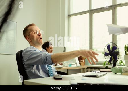 Middle aged Caucasian businessman tossing paper airplane in office, taking break during workday and expressing playful creativity. Useful for teamwork, office culture, productivity Stock Photo
