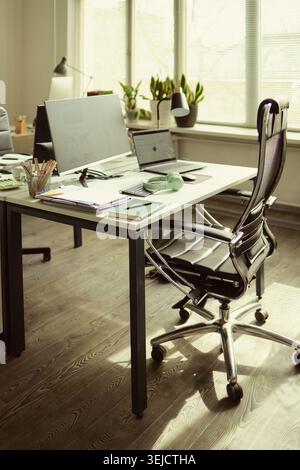 Vertical shot of modern office workstation displaying desktop monitor, laptop, headset, documents, signaling hybrid work setup and productivity. Ideal for remote work or business planning Stock Photo