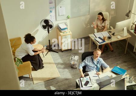 High angle view of diverse office team cooling down with water bottles during heatwave, working at desks and resting. Ideal for workplace wellness, summer productivity, office climate Stock Photo