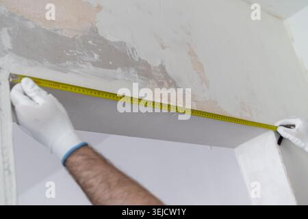 Measuring wall height at construction site using a tape measure. Clean and organized workspace with partially renovated walls visible in background. Stock Photo