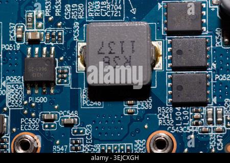 Macro photograph of a blue circuit board focusing on an R36 inductor component, microchips, transistors, and printed labels. (127 characters) Stock Photo