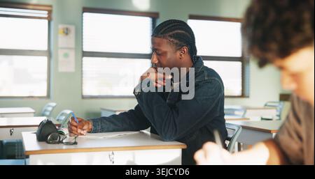 Student, thinking or writing in classroom with college assignment, education or english essay idea. Man, notes or learning in university with problem Stock Photo