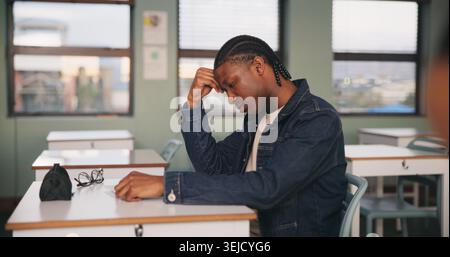 School, bored and tired black man in classroom for lesson, learning and studying at desk. Stress, college and person with fatigue, student or Stock Photo