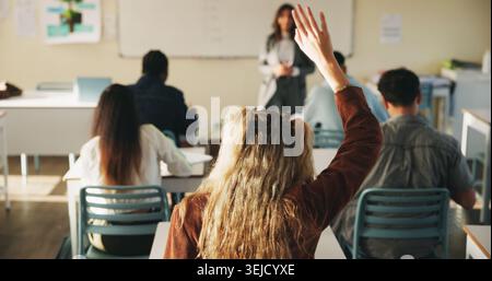Learning, woman and raised hand for question in college, knowledge and development with teacher. Person, education or student ask in lesson, answer Stock Photo