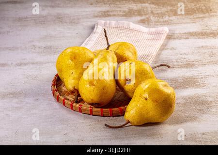 Vibrant yellow pears arranged in natural wicker basket. Rustic wooden background and white cloth complement fresh fruit. Healthy food concept, still l Stock Photo