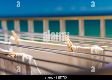 Clothes drying on balcony railing with blurred turquoise ocean background during sunny summer vacation by the sea Stock Photo