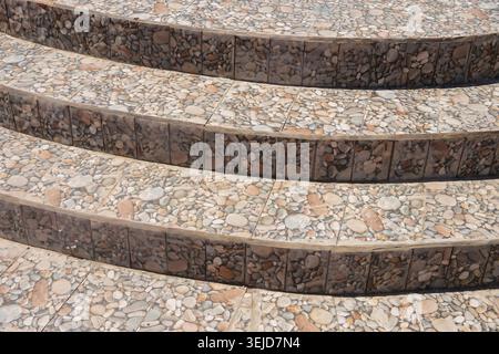 Curved stone steps feature mosaic tiles with pebbles. Brown and beige stones create elegant, textured surfaces. Step edges highlight natural, earthy tones. Ideal for architecture, design Stock Photo