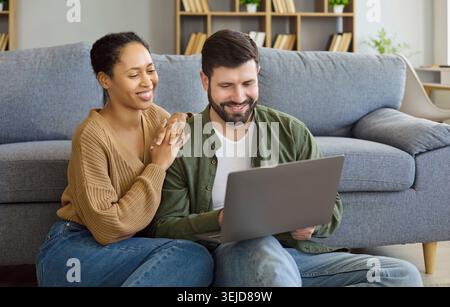 Smiling couple sitting on floor using laptop together in cozy living room Stock Photo