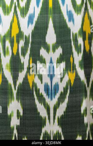 Colorful handwoven ikat textile featuring bold motifs in white, blue, yellow and green. Traditional patterned fabric texture evokes cultural heritage, Stock Photo
