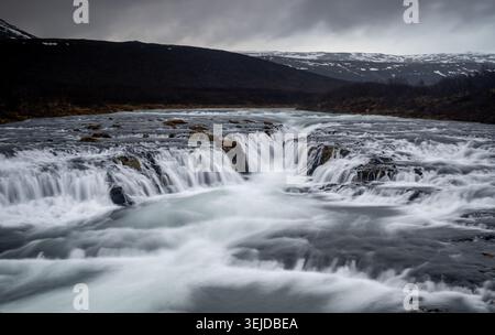 Bruarfoss waterfall showcasing turquoise water cascading over dark rocks in a rugged nordic landscape, Iceland Golden Circle Stock Photo