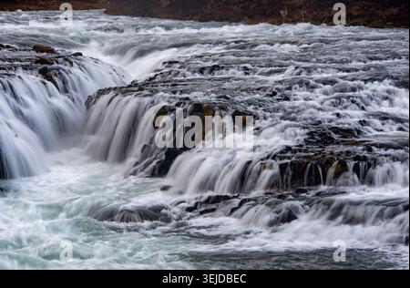 Powerful water surging and cascading over black rocks, showing the strong current of a river in wilderness. Bruarfoss waterfall Iceland Stock Photo