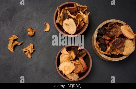 Dried apple pieces in a wooden round plate on a black table, top view Stock Photo