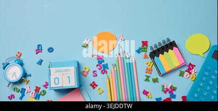 Stationery laid out on a blue background. Multi-colored felt-tip pens, calculator, alarm clock, sticky notes and wooden letters, Stock Photo