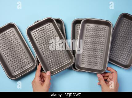 Hand holds black disposable polystyrene foam rectangular plate for packaging vegetables and meat on a blue background Stock Photo