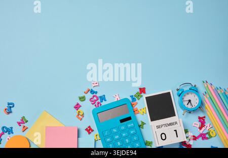 Stationery laid out on a blue background. Multi-colored pencils, calculator, alarm clock, sticky notes and wooden letters, prepa Stock Photo